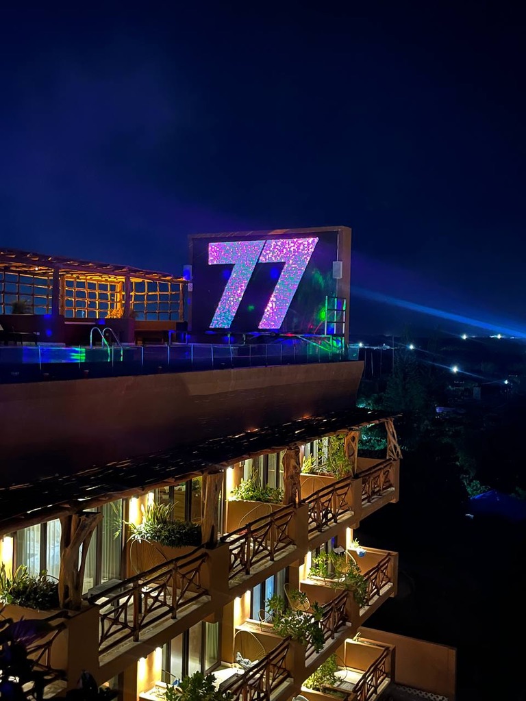 The 77 screen lit over the rooftop pool at night